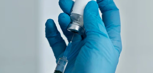 Gloved hand holding a syringe during a vaccination session at Harpley Doctors to promote community immunisation