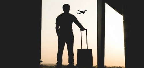 Silhouette of a traveler with suitcase walking through an airport, illustrating Harpley Doctors' travel medicine services